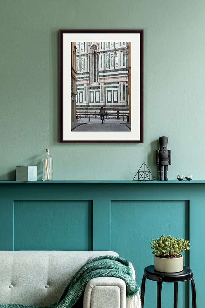The print of a girl riding her bike in front of the Duomo in Florence, Italy, stands in a modern bright living room Captured by Photographer Scott Allen Wilson.