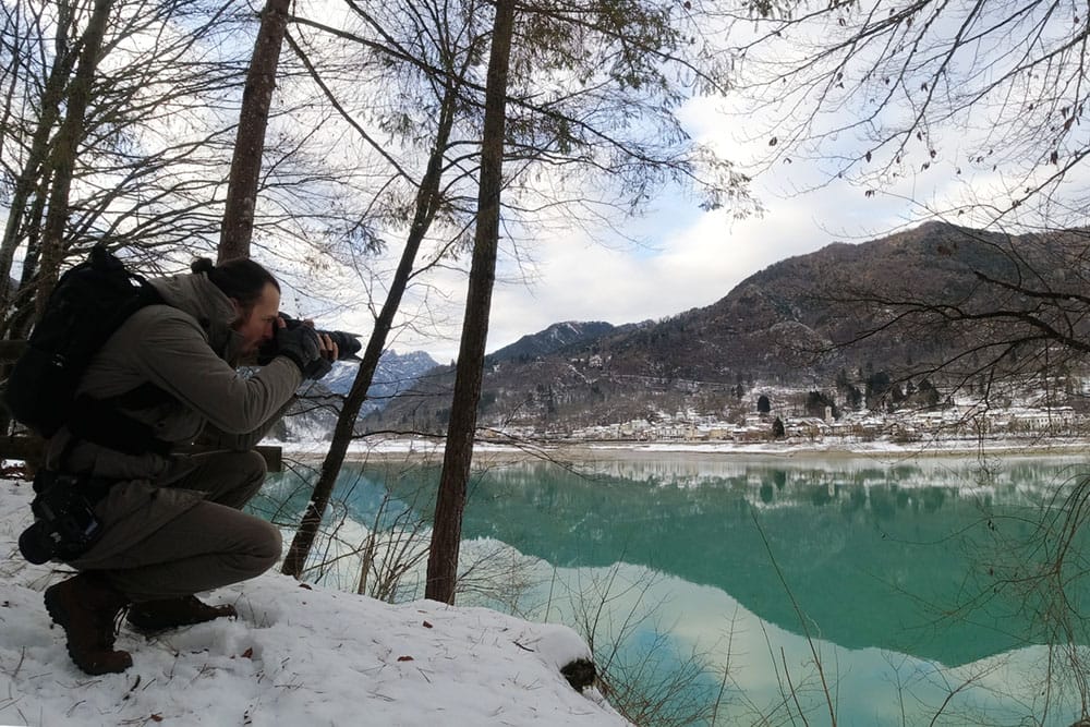 Portrait of photographer Scott Allen WIlson taking a photo in Norhern Italy near a turquoise lake in the snow.