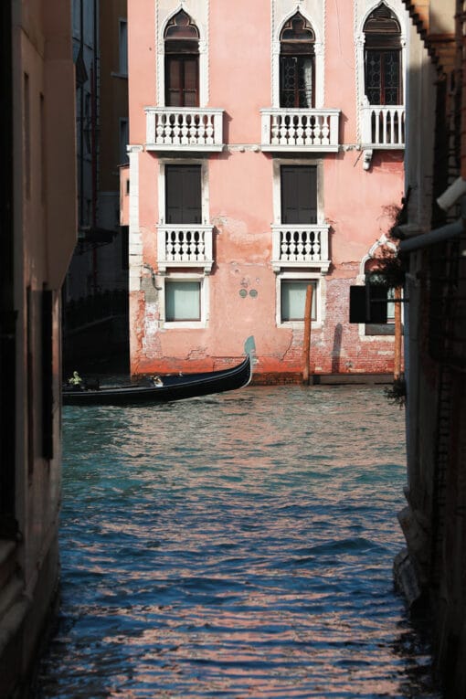 Amazing photo of a narrow waterway in Venice, Italy with a pink building in the background and a gondoliere coming out from the left by Photographer Scott Allen Wilson.