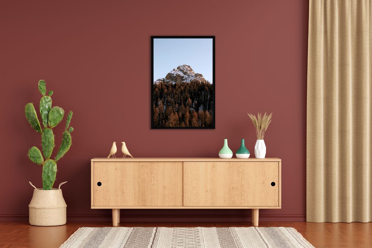Modern shelf decoration with a terracotta wall and a framed photo of a snow-capped mountain of the Dolomites, Italy surrounded by reddish trees taken by Photographer Scott Allen Wilson.