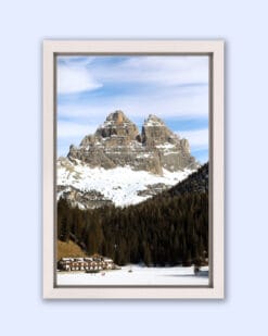 Beautiful white framed landscape photography of the tall Dolomites mountain range in Italy with a forest and houses below, taken by Photographer Scott Allen Wilson.