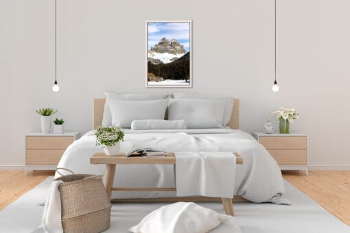 Minimalist bedroom decoration in beige tones with a white framed landscape photography of the tall Dolomites mountain range in Italy with a forest and houses below, taken by Photographer Scott Allen Wilson.