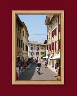 Colorful framed print of a man riding a bike in a street of Lazise, Italy taken by Photographer Scott Allen Wilson.