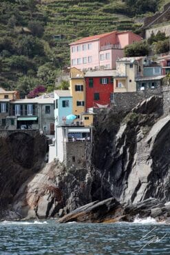The bright tinted houses of Cinque Terre overhanging the rocks are a splash of color in a picture-perfect summer day in Liguria. By Photographer Scott Allen Wilson.