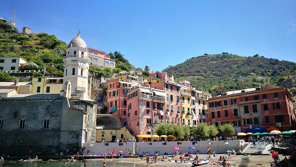 A view of the beach in Vernazza, with people sunbathing and colorful buildings