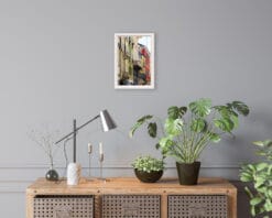 A print of colorful buildings of Parma hung in a room with minimal wooden decor and house plants. By Photographer Scott Allen Wilson.