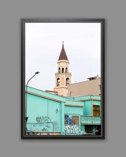 A black framed print of a clock tower emerging from the back of a bright turquoise building covered in graffiti in Pescara, Italy. By Photographer Scott Allen Wilson.