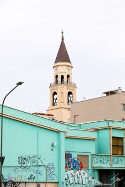 A shot of a clock tower emerging from the back of a bright turquoise building covered in graffiti in Pescara, Italy. By Photographer Scott Allen Wilson.