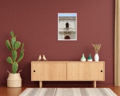 A white framed print of a liberty style building Pescara, Italy hanging in a room with plants and wooden decor. By Photographer Scott Allen Wilson.