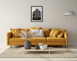 A black framed print of a dystopian steel building in Pescara, Italy, hanging in a traditional style living room with a yellow sofa. By Photographer Scott Allen Wilson.
