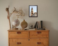 Black framed print of a clock tower at dawn in Pescara, Italy, hanging in a room with natural wood decor and beige decorations. By Photographer Scott Allen Wilson.