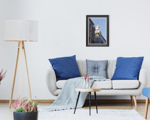 A black framed print of a clock tower in Pescara, Italy, standing out behind modern buildings hanging in a living room with white walls and accents of blue decor. By Photographer Scott Allen Wilson.
