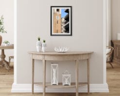 A black framed print of a clock tower in Pescara, Italy, hanging in a neutral room with wooden decor. By Photographer Scott Allen Wilson.