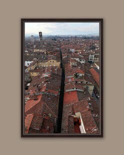 A dark brown framed print of red tiled rooftops in the city of Lucca, Italy, with some bell towers visible. By Photographer Scott Allen Wilson.