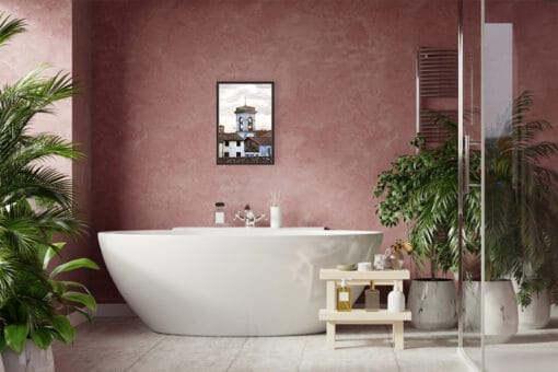 A dark brown framed print of a bell tower and red tiled rooftops in Lucca, Italy, hanging in a boho bathroom. By Photographer Scott Allen Wilson.