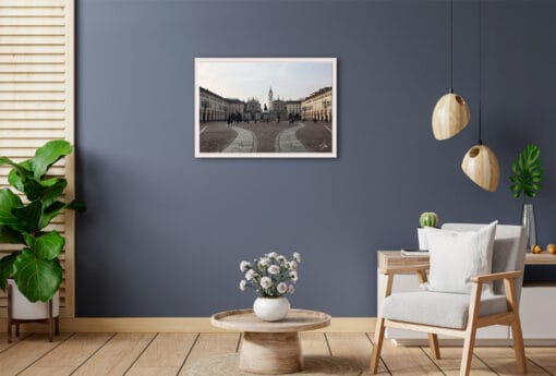 A framed print of San Carlo square in Torino, Italy, hanging in a living room with natural wooden decor.