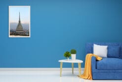 A white framed print of the Mole Antonelliana in Torino, Italy, hanging in a modern living room with blue decor. By Photographer Scott Allen Wilson.