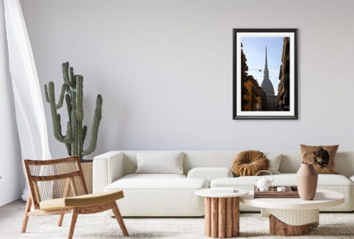 A black framed print of a view of the Mole Antonelliana in Torino, Italy, hanging in a minimal living room wit wooden decor. By Photographer Scott Allen Wilson.