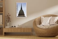 A white framed print of the Mole Antonelliana in Torino, Italy, hanging in a minimal living room with wooden decor. By Photographer Scott Allen Wilson.