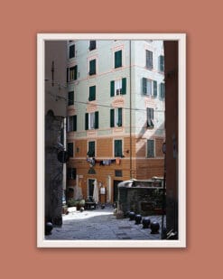 White framed artistic print of a gorgeous alley in Genova, Italy, showcasing the vibrant colors of a building along a downhill cobblestone street. Photo captured by Travel Photographer Scott Allen Wilson.