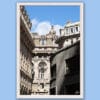 Wooden framed artistic print of a Genovese street scene, where grand adorned structures stand behind a curved, modern one and under a bright blue sky.