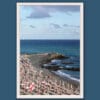 Wooden framed artistic print of a natural landscape, showcasing an empty beach in Genova, where a rocky shore and a blue sea are bathed in soft sunlight.