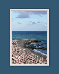 Wooden framed artistic print of a natural landscape, showcasing an empty beach in Genova, where a rocky shore and a blue sea are bathed in soft sunlight.