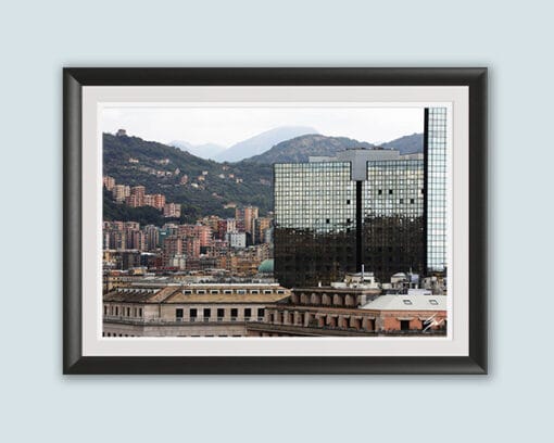 A black frame with a white passe-partout surrounds a work of art created by Travel Photographer Scott Allen Wilson. The subject is a landscape of Genova, Italy, which focuses on a mix of historical buildings, and a reflective modern skyscraper as well.