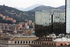 A glass skyscraper highlights a view of Genova’s countryside, from a viewpoint within Genova’s historical center. The photo is framed and matted with a black frame and white passe-partout.