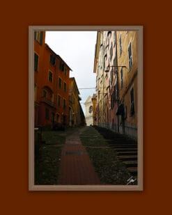 Wooden framed artistic print of some houses in the outskirts of the city. A steep alley climbs towards the skies, while a soft warm light surrounds the whole image.