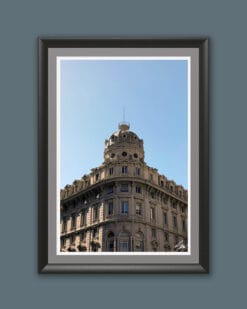 A black wooden framed piece of art of a gorgeous historical construction, filled with windows and decorative details, stands proud beneath a serene blue backdrop.