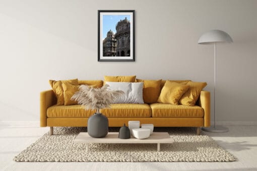 A few grey and white vases decorate the table of this brightly lit living room. The color matches with the dark frame and white passe-partout surrounding the image. In the latter, deep shadows are cast on the walls of the monuments, creating a beautiful tonality contrast with the mustard yellow sofa.