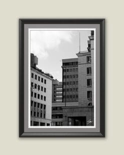 Wooden framed piece of art by Travel Photographer Scott Allen Wilson, featuring a black and white cityscape with tall blocks and linear windows.