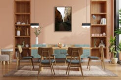 The walnut frame of this warm toned picture matches the textures of a dining room, where natural wood furnishings predominate. The earthy colors of the buildings harmonize the warmth of the peachy walls and the wooden decors, while some plants resemble the touch of green on the alley.